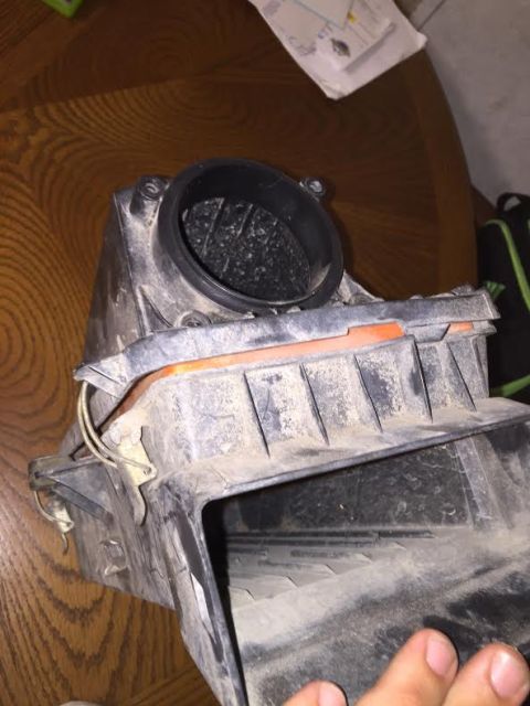 1996 Ford Bronco - A dusty black plastic air intake box with an orange seal is shown on a wooden table. The interior of the box appears to have a mesh or filt…