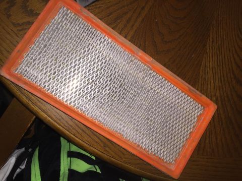 1996 Ford Bronco - A rectangular air filter with an orange rubber seal is shown resting on a wooden table. The filter media is a white pleated material with a…