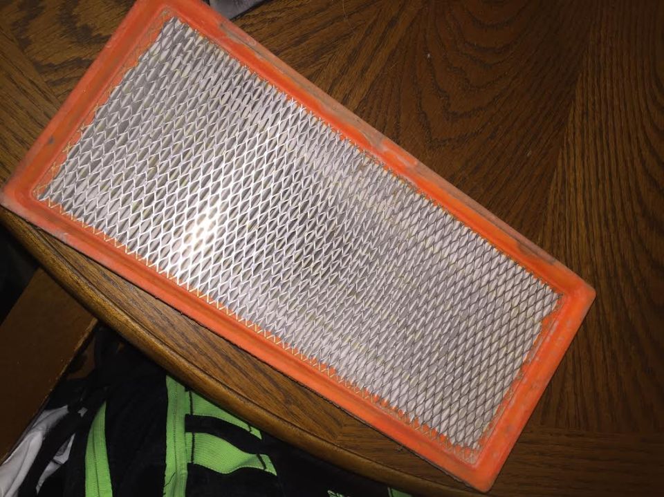 Rectangular air filter with orange seal on a wooden table.