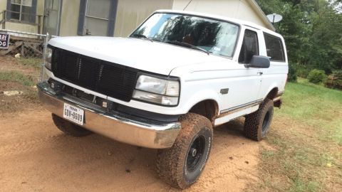 1996 Ford Bronco - A white 1996 Ford Bronco, nicknamed "The Yeti", is parked on a dirt path in front of a house. The vehicle has a black grille, chrome bumper…