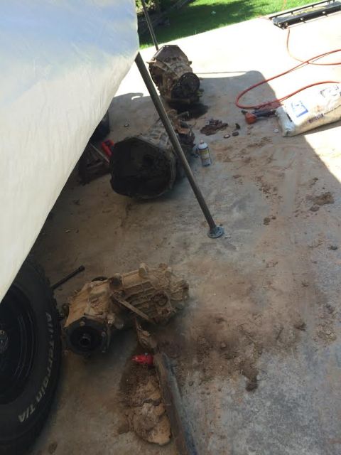 1996 Ford Bronco - Two transfer cases and a transmission are laid out on a concrete surface next to a large white tarp. One transfer case is partially obscure…