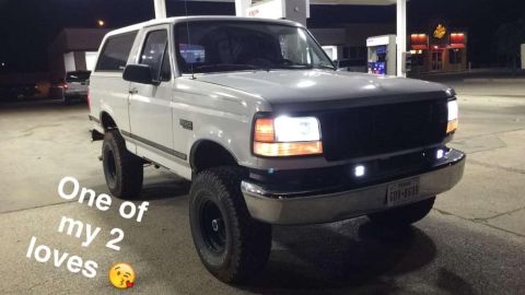 1996 Ford Bronco - A white 1996 Ford Bronco is parked at a gas station at night. The vehicle has aftermarket lights on the front bumper and is lifted with lar…