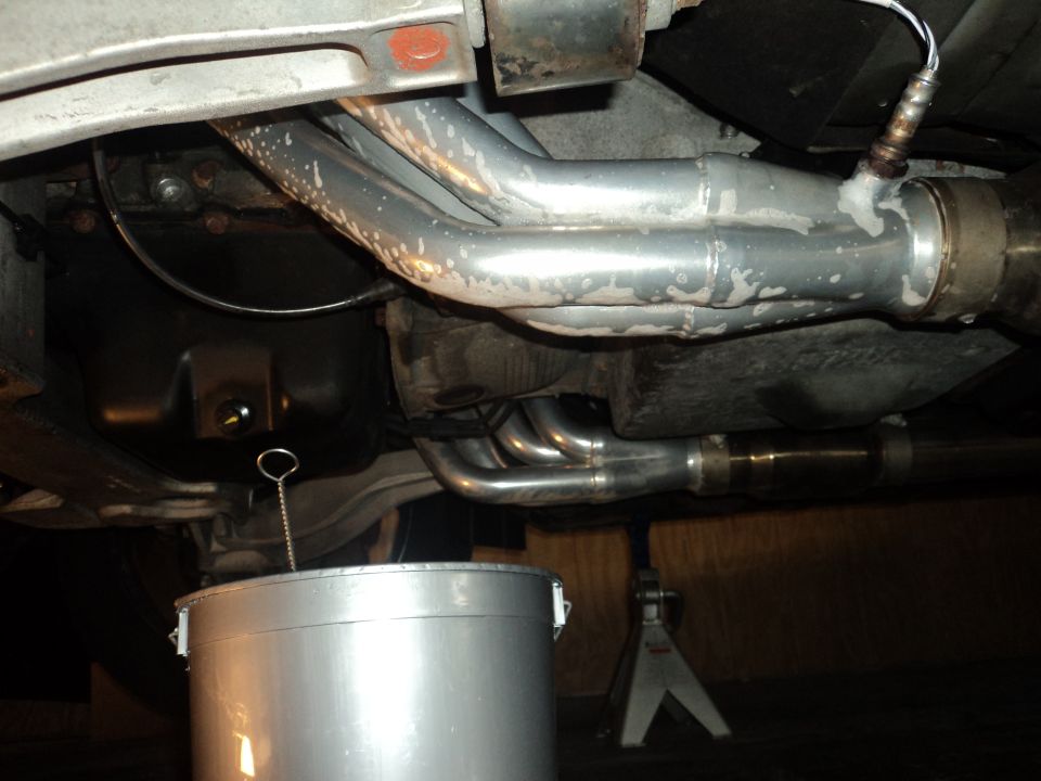 Vehicle oil pan and exhaust system with oil drain bucket below.