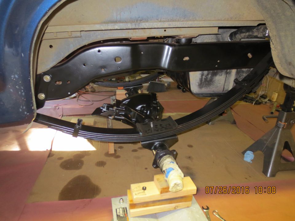 Underside of a vehicle showing rear axle, leaf springs, and fuel tank.