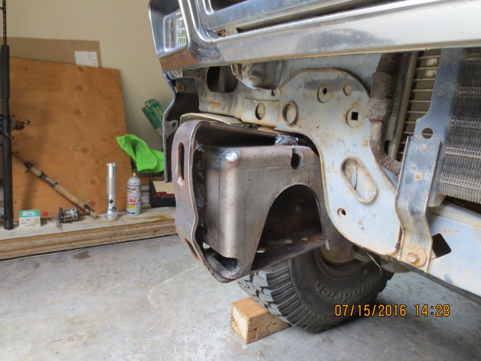 Welded bracket on vehicle frame near tire and radiator, with tools in background.