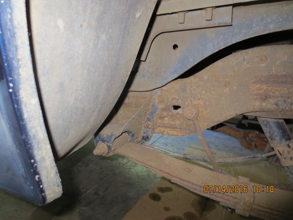 Undercarriage of a vehicle showing rusted leaf spring and blue fender.