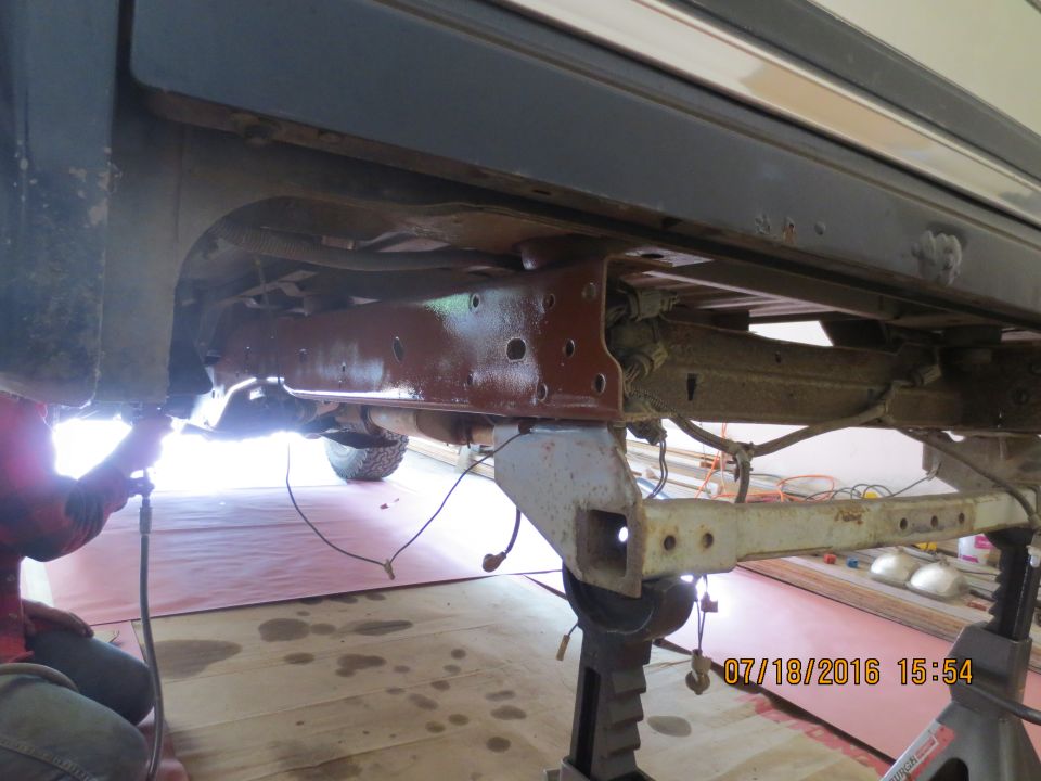 Underside of a vehicle frame being worked on, painted reddish-brown.