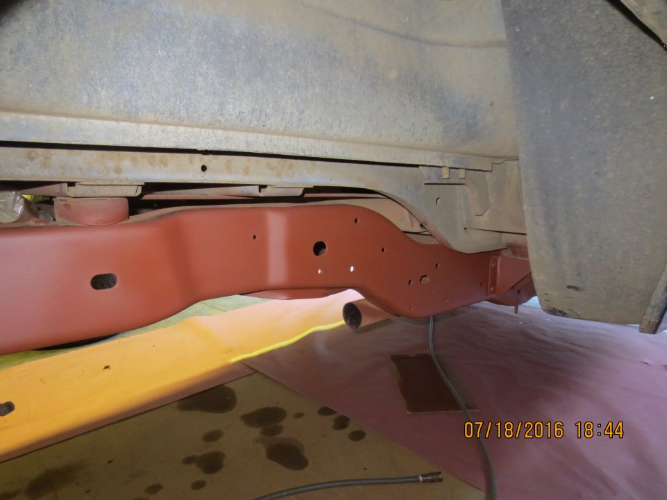 Reddish-brown primed vehicle frame underside with tire visible.