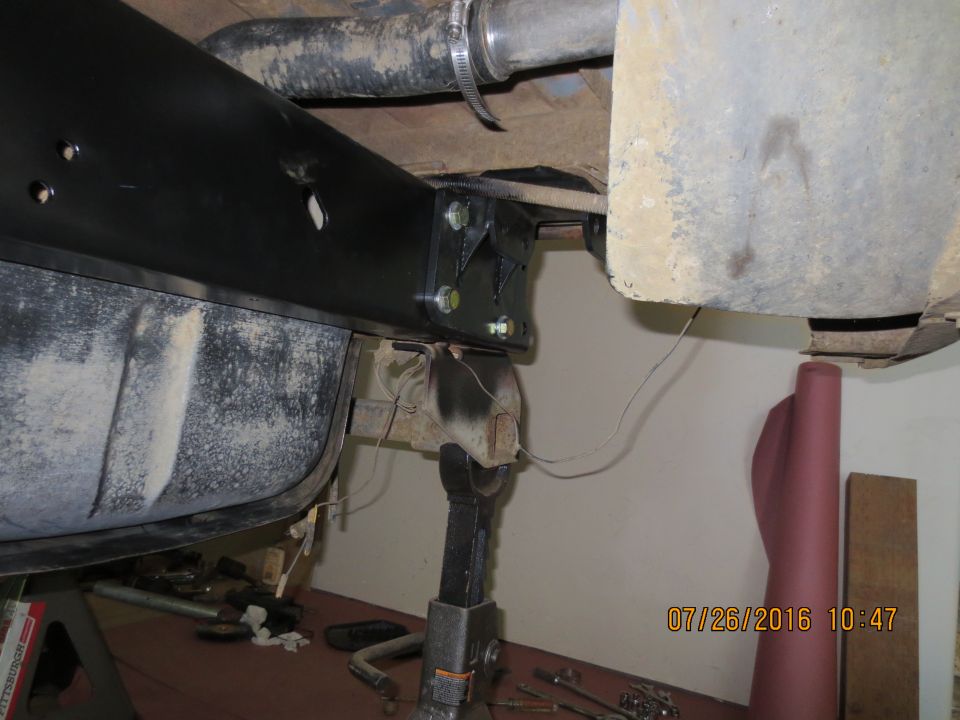 Vehicle frame with fuel tank, exhaust pipe, and aftermarket reinforcement bracket. Jack stand visible.