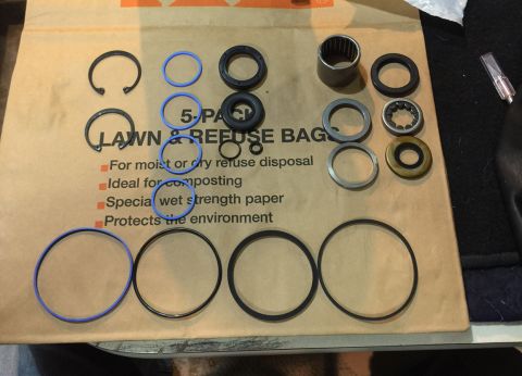 1978 Ford Bronco - A collection of various metal and rubber rings, seals, and a bearing are laid out on a brown paper bag. The bag has text that reads "LAWN &…