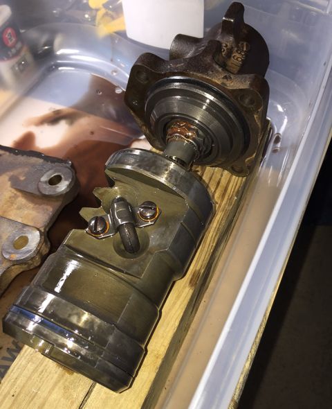 1978 Ford Bronco - A disassembled automotive part, likely a power steering pump, sits in a clear plastic container with some fluid. The part is made of metal…