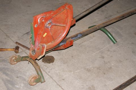 1979 Ford Bronco - A close-up view of an orange implement with metal arms and wheels, resting on a concrete surface. A mallet is visible to the left of the im…