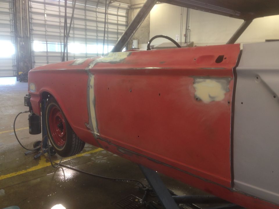 Red classic car fender and door with body filler in a garage.