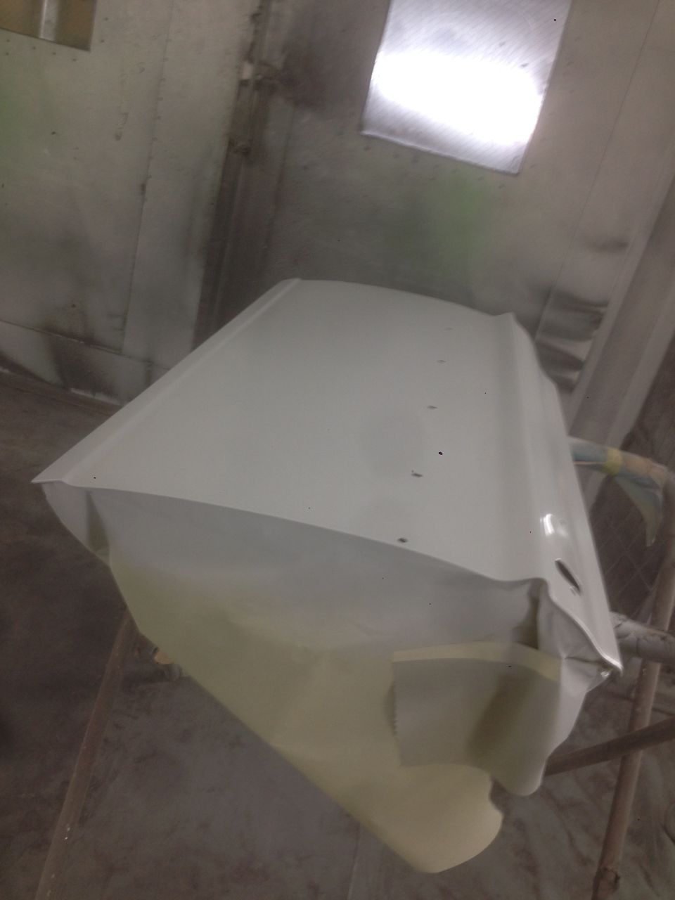White car door being masked for paint inside a spray booth.