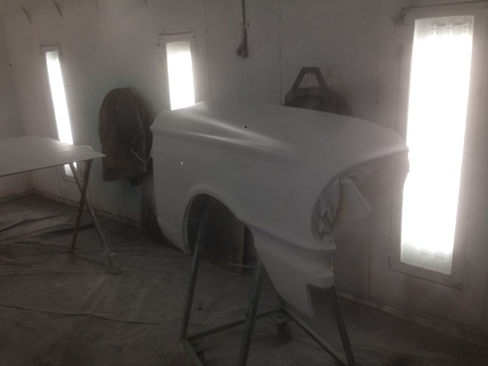 White car fender in primer on a stand in a paint booth.