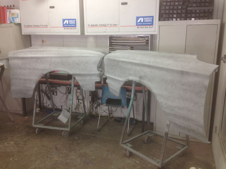 Two car fenders covered in protective material on stands in a workshop.