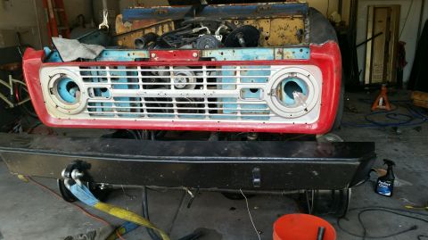 1979 Ford Bronco - The front end of a vintage Ford Bronco is shown in a garage setting, with the grille and red fender trim visible. A black aftermarket bumpe…