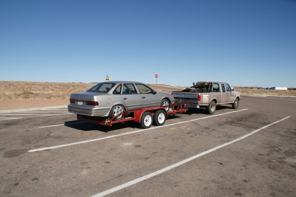 Silver sedan on a red trailer being towed by a light brown pickup truck.