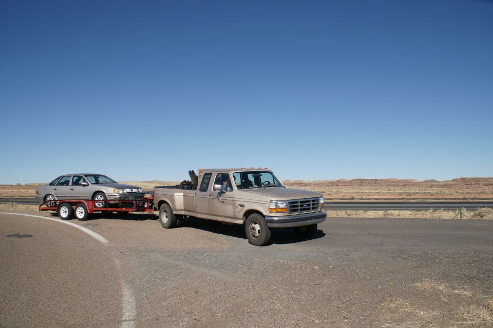 Tan Ford F-350 dually truck towing a silver sedan on a trailer.