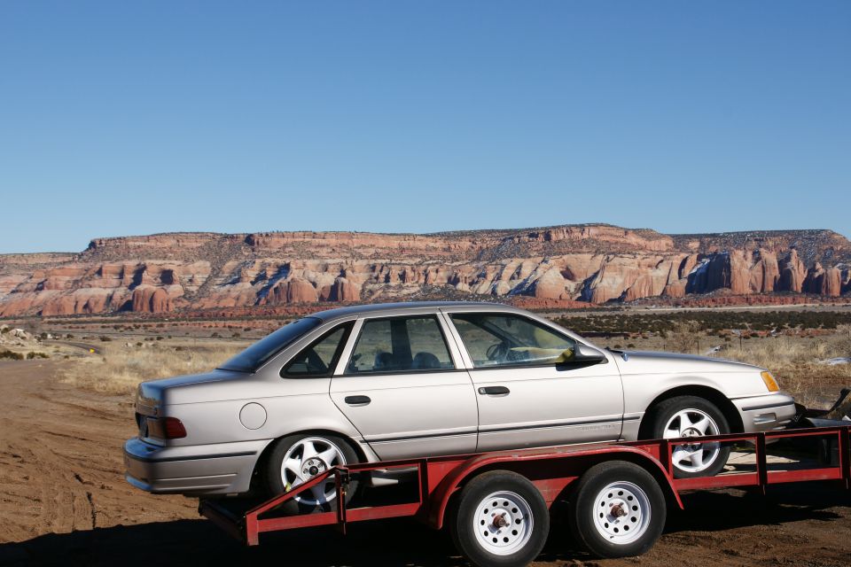 Silver sedan on a red car trailer with desert mountains in the background.