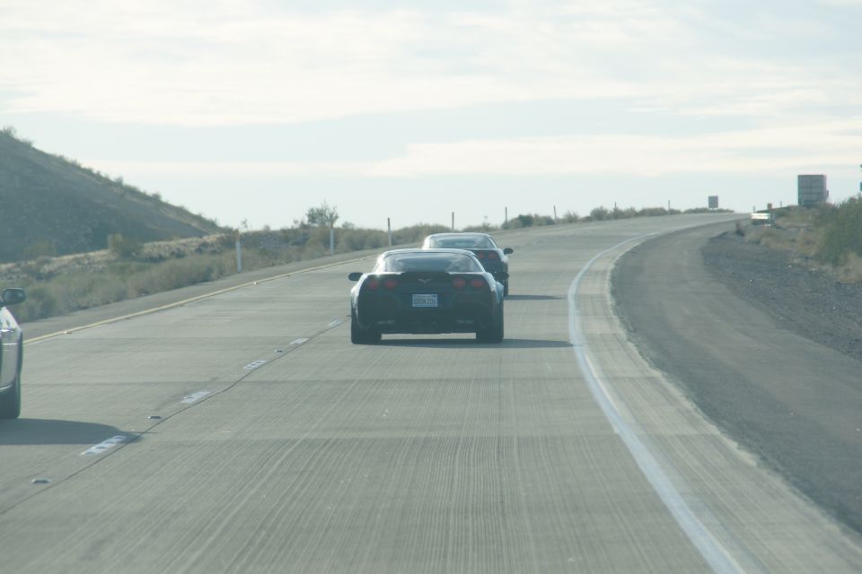 Two black Chevrolet Corvettes driving on a highway.