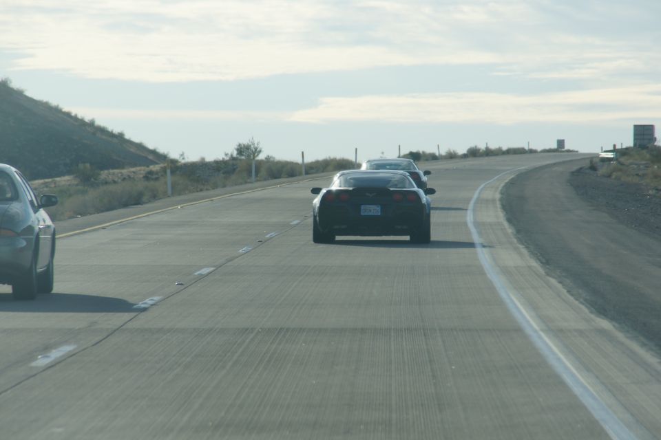 Two black Chevrolet Corvettes on a highway in a desert landscape.