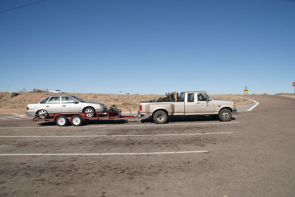 Silver sedan on a trailer towed by a beige pickup truck.