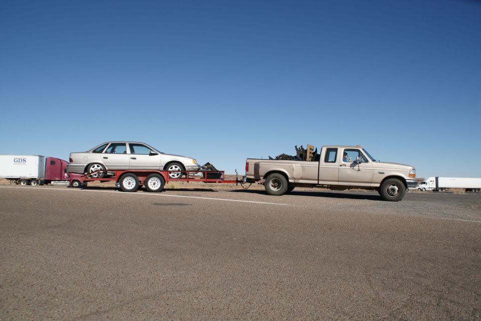 Gold pickup truck towing a car on a trailer, with a semi-trailer truck in the background.