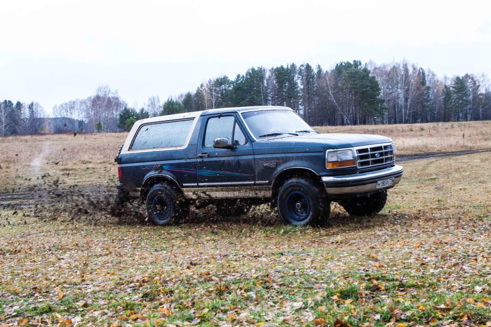 Dark blue Ford Bronco driving through mud with trees in the background.