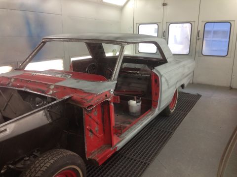1964 Ford Fairlane - A classic car is prepped for paint in a booth, showing its stripped interior and body panels.