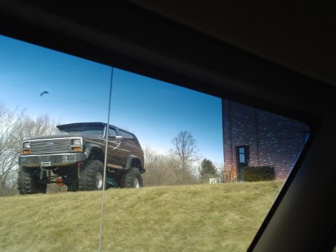 1993 Ford Bronco - This lifted 1993 Ford Bronco sits on a grassy incline under a clear blue sky.