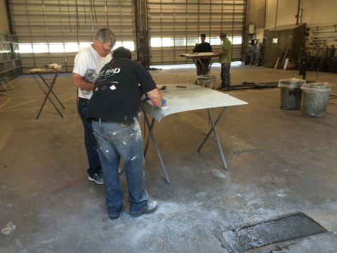 1964 Ford Fairlane - Workers are sanding a car hood in a workshop setting.