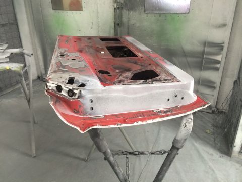 1964 Ford Fairlane - A car door is prepped for painting in a spray booth, showing areas of primer and exposed metal.