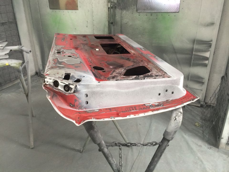 Red car door undergoing bodywork, resting on sawhorses in a paint booth