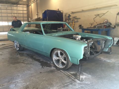 1964 Ford Fairlane - A light blue coupe is in a workshop, missing its front bumper and grille, with a man working on the trunk.