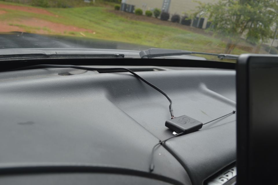 Dashboard of a vehicle with a black GPS device and antenna, showing a portion of the windshield and exterior