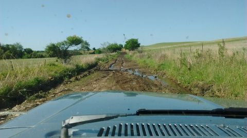 1985 Ford Bronco - View from inside a vehicle as it navigates a challenging, muddy path through a rural landscape.