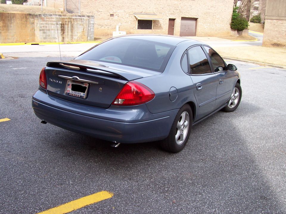 Blue-gray Ford Taurus SE sedan with rear spoiler, seen from rear passenger side in a parking lot