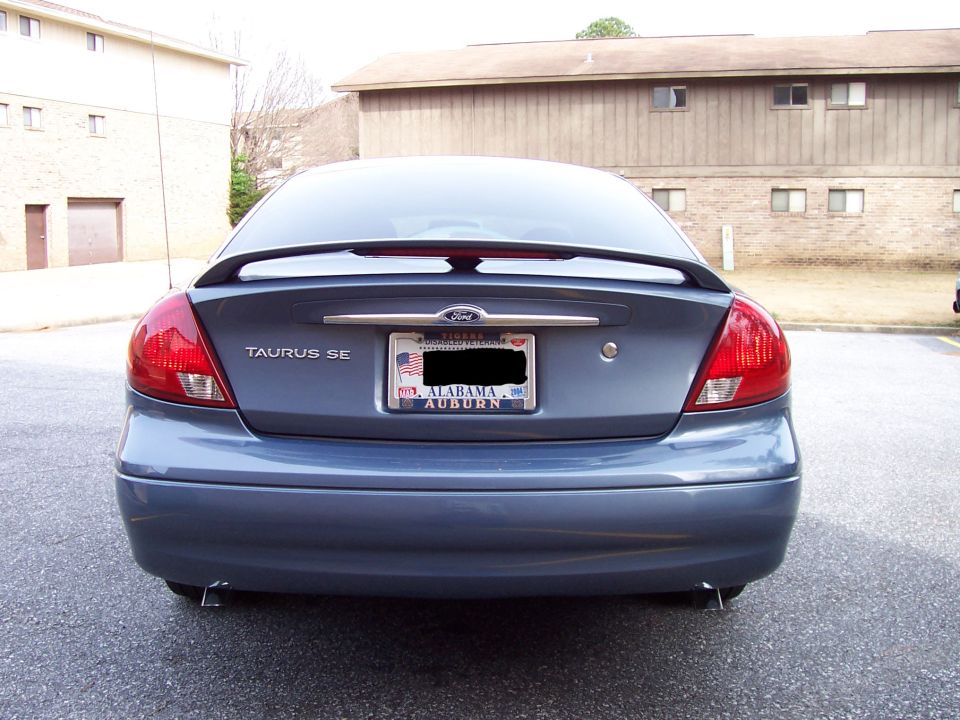 Rear view of blue-gray Ford Taurus SE sedan with spoiler and Alabama plate, parked near apartment buildings