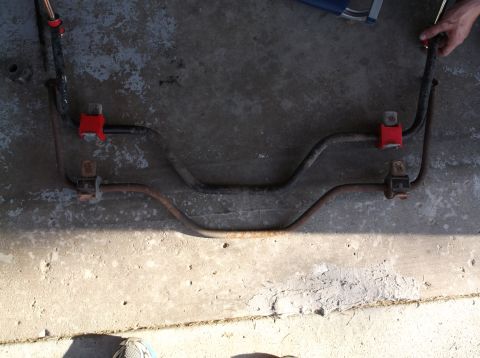 2001 Mercury Grand Marquis - removed anti-roll sway bar with red polyurethane bushing mounts resting on a concrete garage floor.