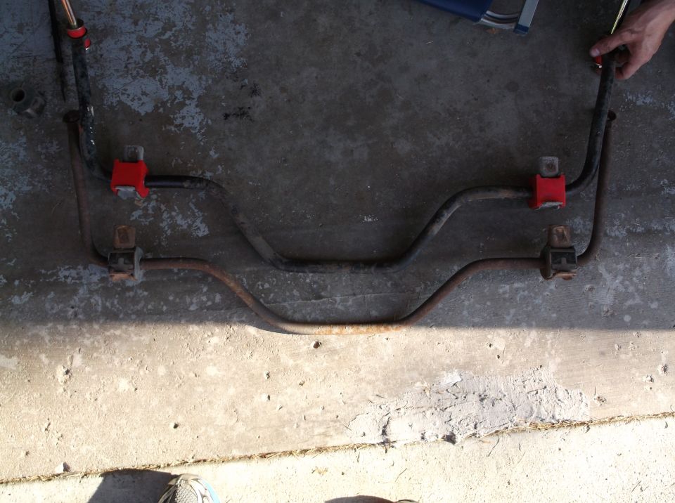 Removed sway bar with red polyurethane bushings lying on concrete floor