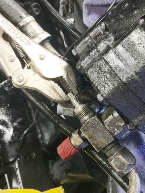 1978 Ford Bronco - Close-up of a mechanic working on a vehicle's engine components with tools.