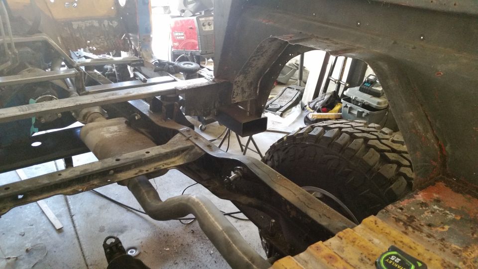 Underbody of a vehicle undergoing repair, showing frame, suspension, and a large tire