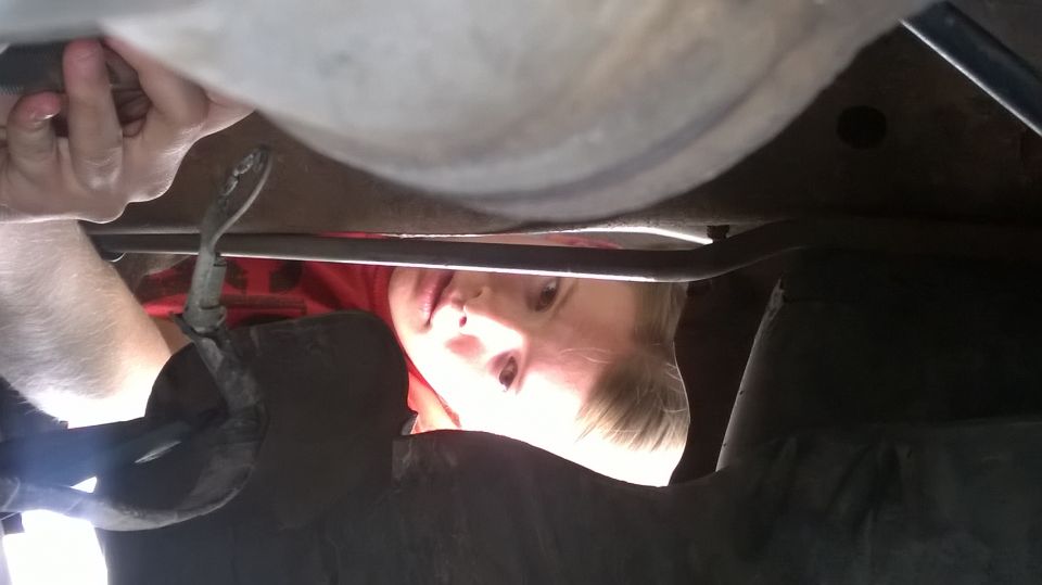 Person lying under a vehicle's undercarriage with a hand reaching up to a part