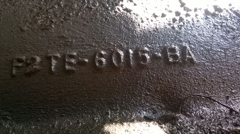 Cast-in Ford part number F2TE-6015-BA on a grimy black cast iron engine block surface