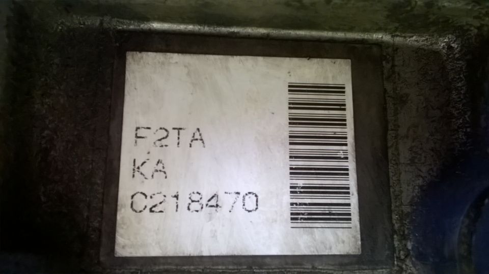 Label with text F2TA, KA, C218470 and a barcode on a dark metal surface