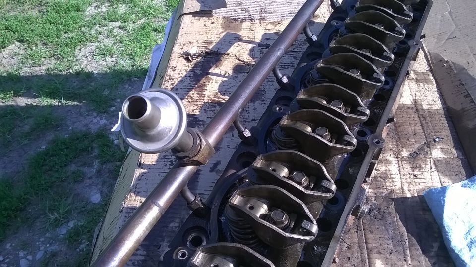 Engine cylinder head with rocker arms and a fuel rail assembly. The head is black and appears to be made of metal