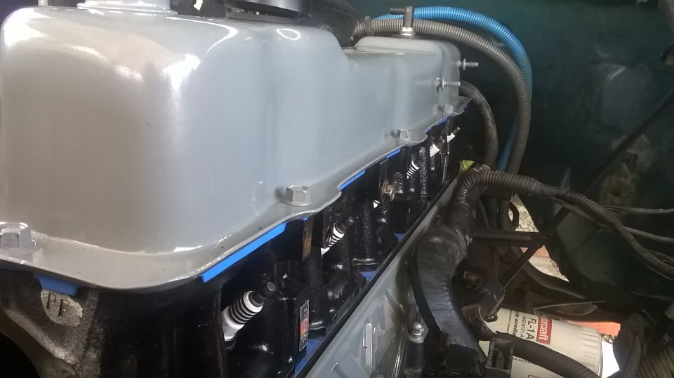 Close-up of engine valve cover and spark plugs with blue gasket material visible