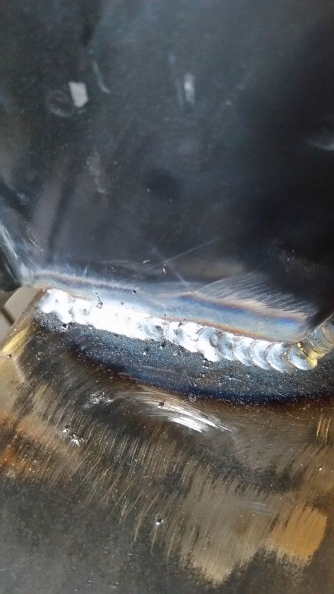 1979 Ford Bronco - A close-up view shows a freshly welded seam on a metal vehicle component. The weld exhibits a rainbow heat tint and some porosity, indicati…