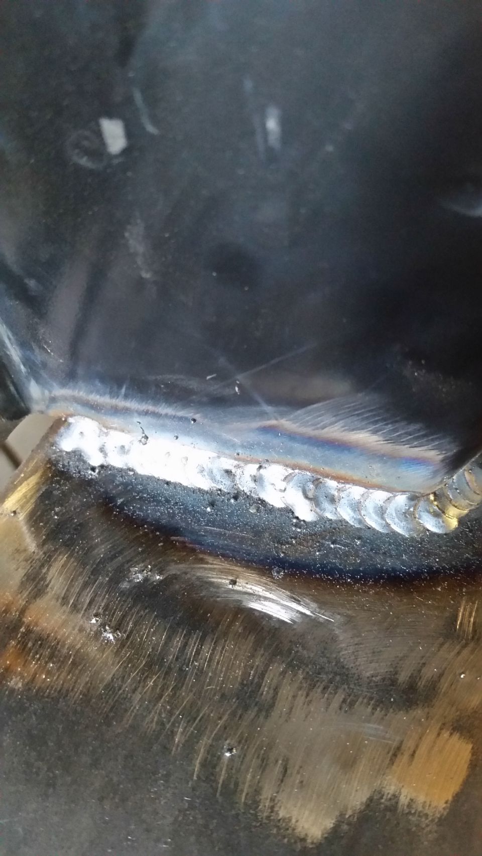 Close-up of a metal weld seam with rainbow heat tint and porosity.